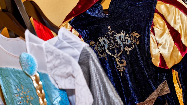 Colorful children's costumes hang on a clothing rack. The outfits are designed in various styles and colors.