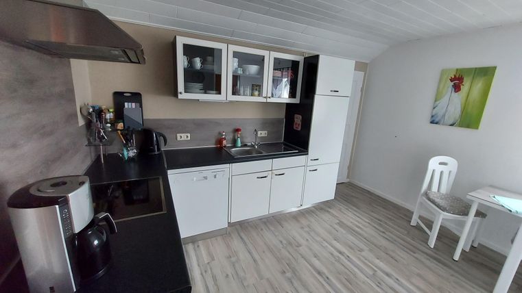 A modern kitchen with a black countertop and white cabinets. On the right side, there is a table and a chair, complemented by a colorful piece of art on the wall.