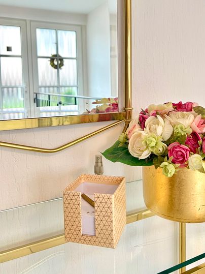 A beautiful room with a golden mirror and a flower vase. A decorative box is on the table.