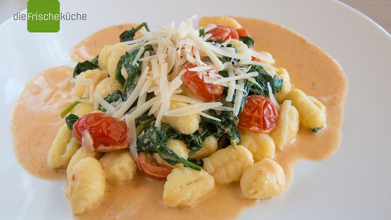 Ein Teller Gnocchi mit Spinat, Kirschtomaten und einer cremigen Sauce. Das Gericht ist mit Käse bestreut und sieht appetitlich aus.