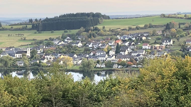 Een schilderachtig landschap met een klein dorp aan de rivier. Omgeven door groene heuvels en bomen.