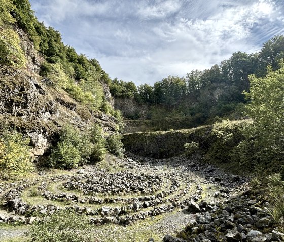 Steinspirale im Arensberg Vulkan, umgeben von bewaldeten Felsw&auml;nden unter einem blauen Himmel mit Wolken., &copy; Touristik GmbH Gerolsteiner Land