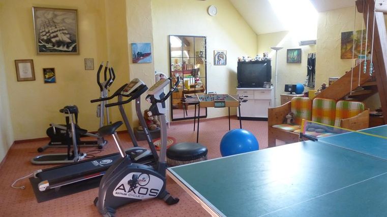 Ein heller Fitnessraum mit verschiedenen Trainingsgeräten und einem Pool-Billardtisch. Der Raum hat große Fenster und eine gemütliche Atmosphäre.
