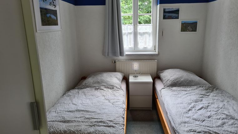 Ein einfaches Schlafzimmer mit zwei Einzelbetten und einem Nachttisch. Die Wände sind hell gestrichen und haben blaue Streifen.