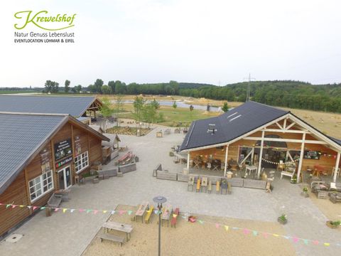 A spacious outdoor area with two wooden buildings, surrounded by green spaces. The place is ideal for events and social gatherings.