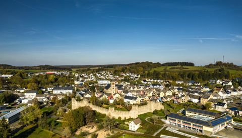 Eine malerische Stadt mit einer historischen Stadtmauer und vielen Häusern. Die Umgebung ist grün und bewaldet, unter einem klaren blauen Himmel.