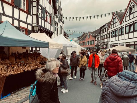Een levendige markt in een charmante oude stad met traditionele vakwerkhuizen. Mensen slenteren tussen de stands en genieten van de sfeer.
