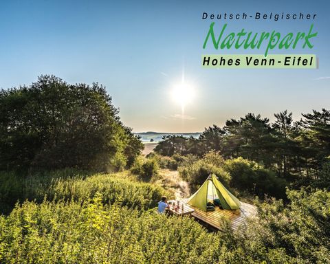 A beautiful view of the Hohes Venn-Eifel Nature Park with a green tent landscape. The sun rises on the horizon and illuminates the surroundings.