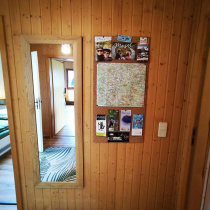 Een hal met houten paneelwanden, een spiegelwand en een informatiebord. Het bord toont kaarten en brochures over verschillende activiteiten.