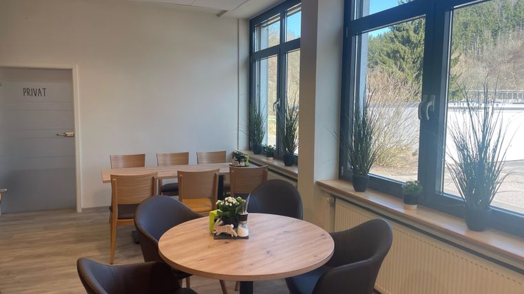 Een gezellige vergaderruimte met een ronde tafel en zwarte stoelen. Grote ramen zorgen voor veel daglicht en een vriendelijke sfeer.