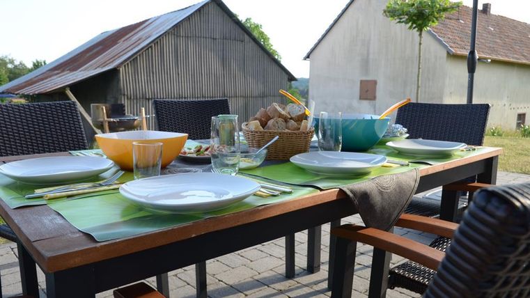A beautiful table outdoors, set with dishes and glasses. In the background, rural buildings can be seen.