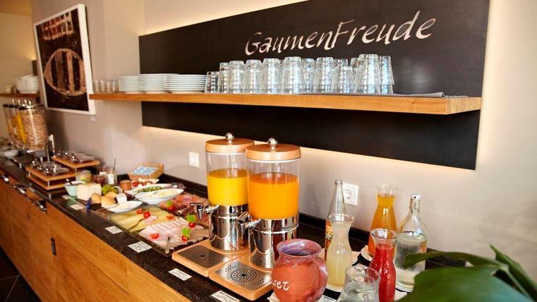 Een uitnodigend ontbijtbuffet met verschillende gerechten en dranken. Op de voorgrond staan twee sapdispensers en verse ingrediënten op een tafel.