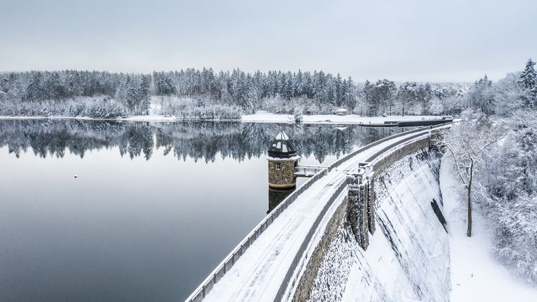 Winterse Dreilägerbach-stuwdam met besneeuwd landschap en rustig water.