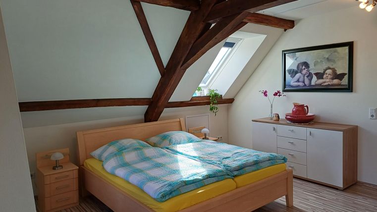 A bedroom with a large bed and colorful blankets. The walls are slanted, and there is a wooden wardrobe as well as a picture on the wall.