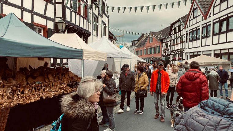 Ein lebendiger Markt in einer charmanten Altstadt mit traditionellen Fachwerkhäusern. Menschen schlendern zwischen den Ständen und genießen die Atmosphäre.