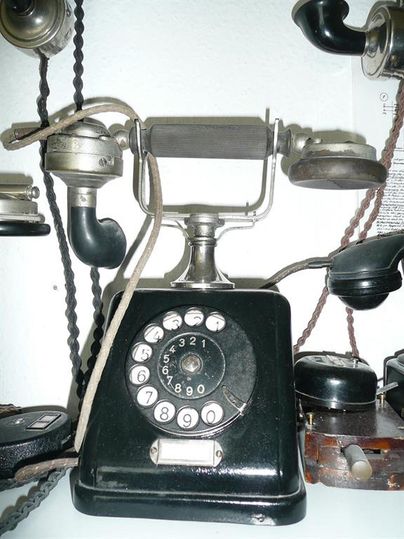 Ein antikes schwarzes Wählscheibentelefon mit Hörer und Kabeln, ausgestellt im Telefonmuseum Gerolstein.