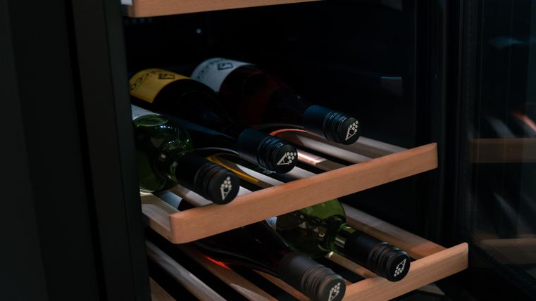 Ein Weinschrank mit mehreren Flaschen Wein auf Holzregalen. Die Flaschen sind klar sichtbar und in verschiedenen Farben.