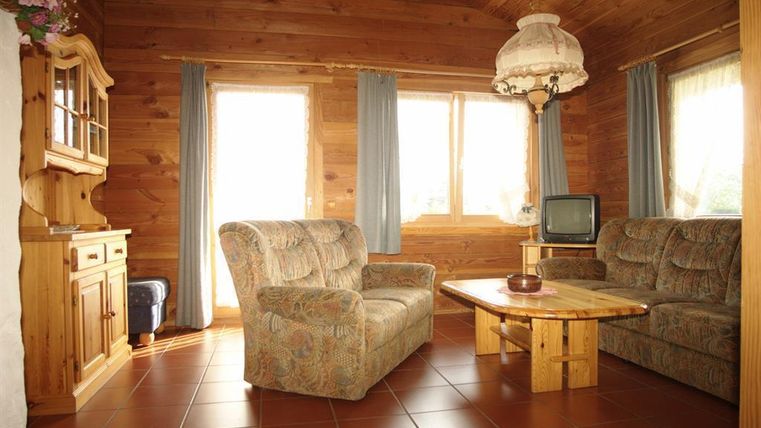 Ein gemütliches Wohnzimmer mit Holzwänden und großen Fenstern. Es gibt zwei Sofas, einen Holztisch und einen Fernseher.