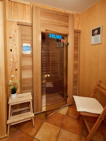 Interior view of a sauna room with wooden walls, a glass door with the inscription 'Salina Vita', a chair, and decorations.