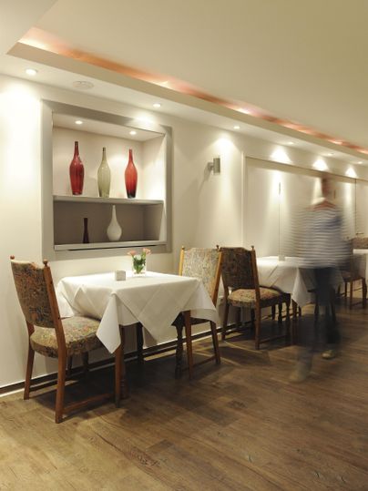 Ein elegantes Restaurant mit gut gedeckten Tischen und warmem Licht. An den Wänden sind dekorative Vasen arrangiert.