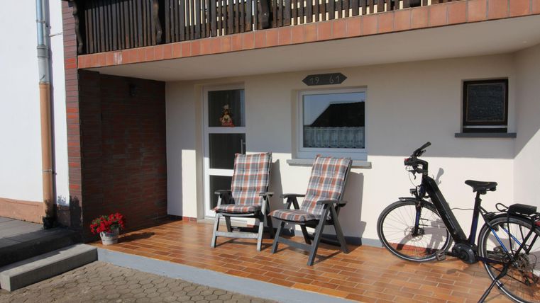 Een balkon met twee gezellige ligstoelen en een fiets. De houten oppervlakte en de bloeiende planten geven de plek een uitnodigende sfeer.