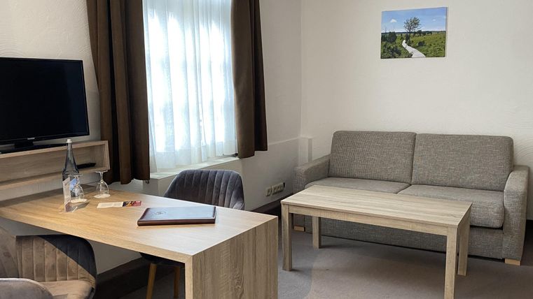 Ein modernes Zimmer mit einem Sofa, einem Tisch und einem Fernseher. Lichtstrahlen fallen durch das Fenster und ein Bild hängt an der Wand.