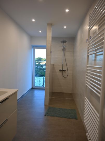 Een modern badkamer met een douche en grote tegels. Een raam zorgt voor veel daglicht en uitzicht naar buiten.