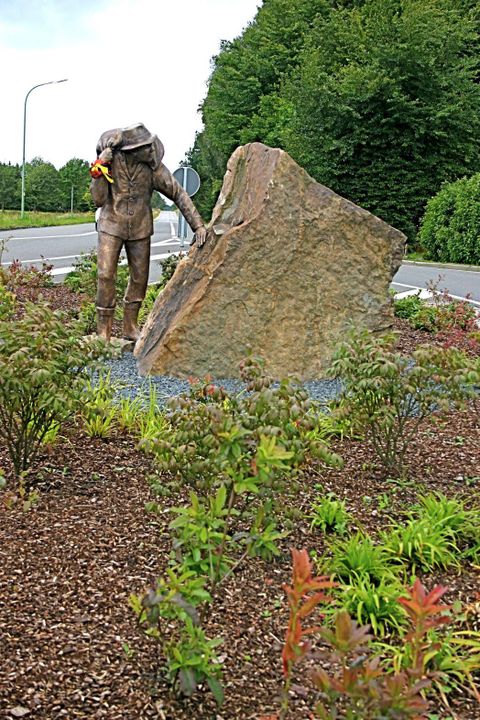 A statue of a diver interacting with a large stone. Surrounded by colorful plant arrangements.