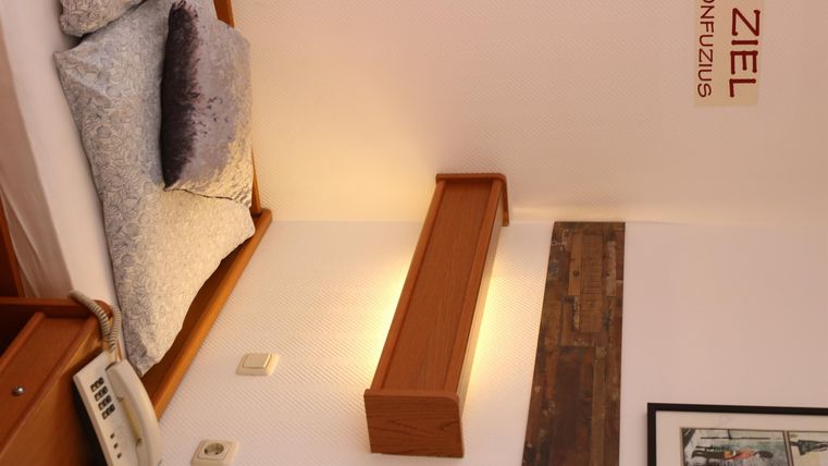 Ein gemütliches Schlafzimmer mit Holzdetails und sanfter Beleuchtung. Die Wände sind neutral gestaltet, und es gibt Kissen auf dem Bett.
