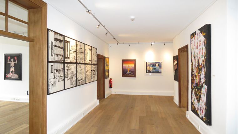 Ein moderner Ausstellungsraum mit Holzfußboden. An den Wänden hängen verschiedene Kunstwerke.