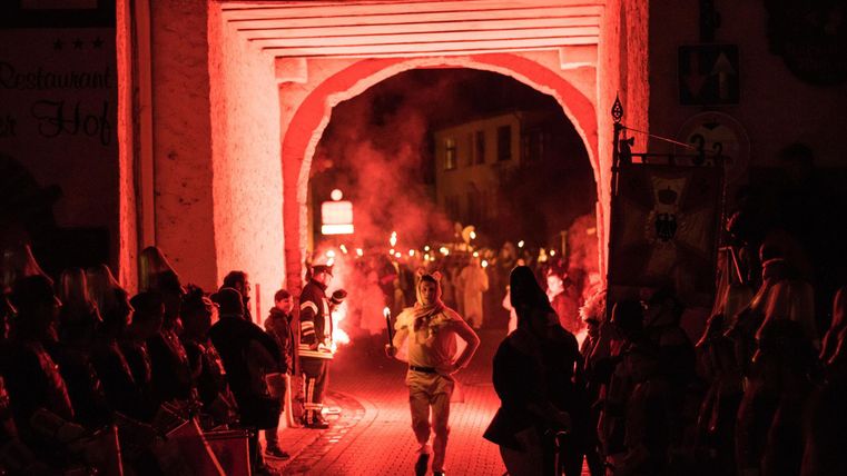 A festive scene with people celebrating a traditional event. Red lights and torches create a celebratory atmosphere in the entrance area.