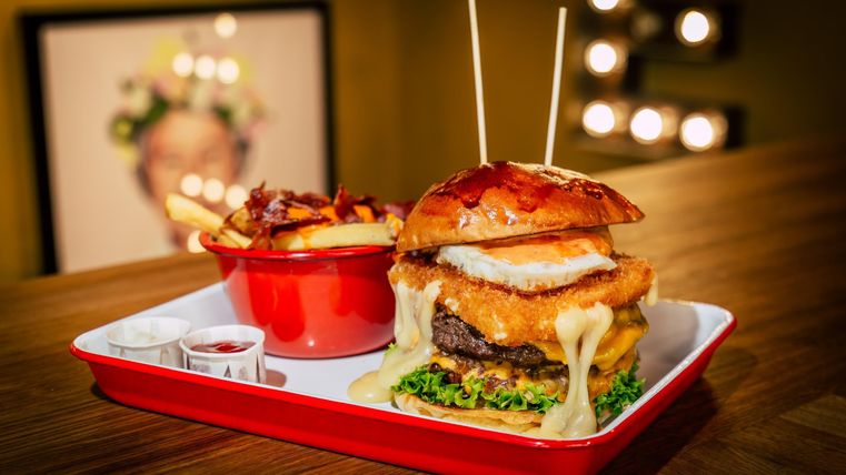 Een sappige burger met kaas, sla en een krokante bun. Daarbij een kom met frietjes.