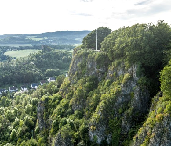 Luftaufnahme der Munterley Felsen bei Gerolstein. Bewaldete Klippen erheben sich über ein Tal mit Häusern. Im Hintergrund sind Hügel und Wälder zu sehen., © Eifel Tourismus GmbH, Dominik Ketz