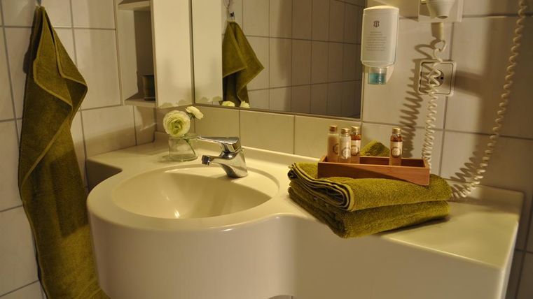 Ein modernes Badezimmer mit einem weißen Waschbecken und grünen Handtüchern. Auf dem Waschbecken steht ein Tablett mit Pflegeprodukten.
