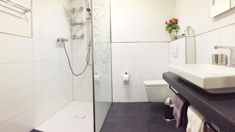 Ein modernes Badezimmer mit einer Glasdusche und eleganten Fliesen. Auf dem Waschtisch steht eine kleine Blumendekoration.