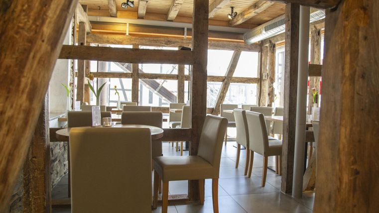Een gezellig restaurant met houten balken en elegante tafels. De grote raampartij zorgt voor veel licht en een uitnodigende sfeer.