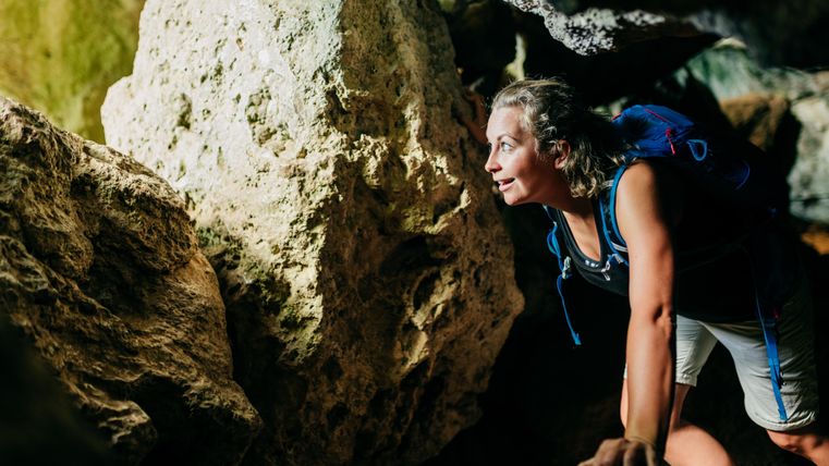 Eine Person erkundet eine Höhle und klettert über große Felsen. Es ist eine spannende und abenteuerliche Umgebung mit natürlichem Licht.