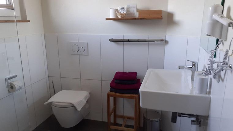 Ein modernes Badezimmer mit einem Waschbecken und einer Toilette. Handtücher liegen auf einem Holzregal in der Nähe.