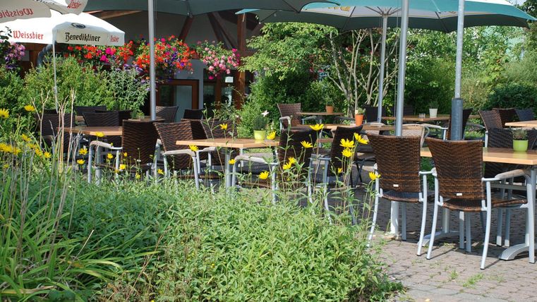 A cozy outdoor area with tables and chairs under sun umbrellas. Surrounded by colorful flowers and green vegetation.
