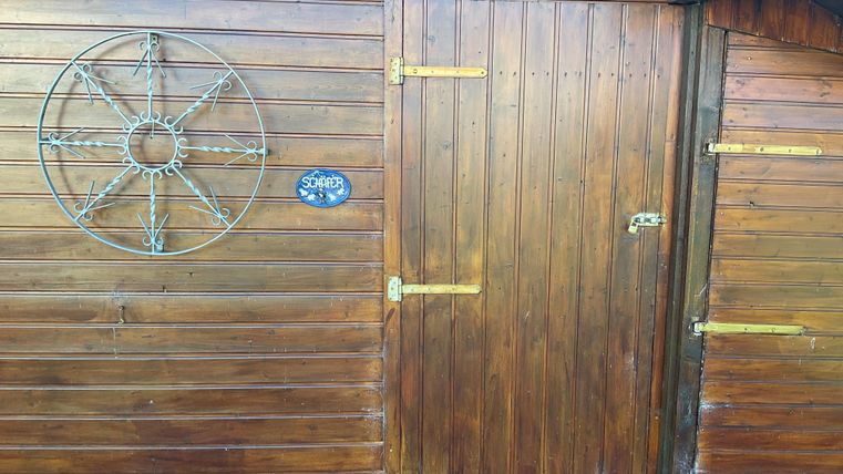 A wooden door with a star wheel and a small sign. The surface is dark brown and showcases the natural wood grain.
