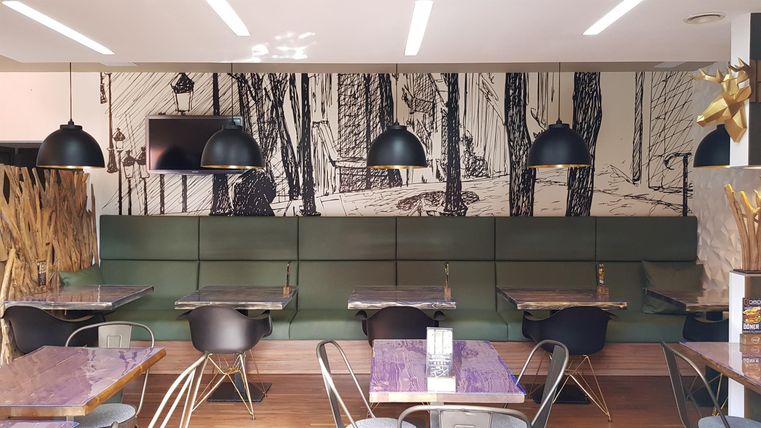 Een modern etablissement met stijlvolle tafels en stoelen. De muren zijn versierd met een artistieke weergave van bomen.
