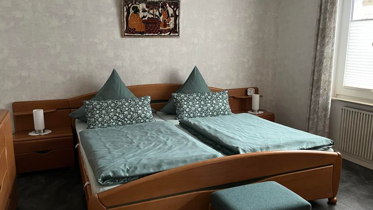 Ein gemütliches Schlafzimmer mit zwei Einzelbetten und blauen Kissen. Die Wände sind hell und mit einem dekorativen Bild geschmückt.