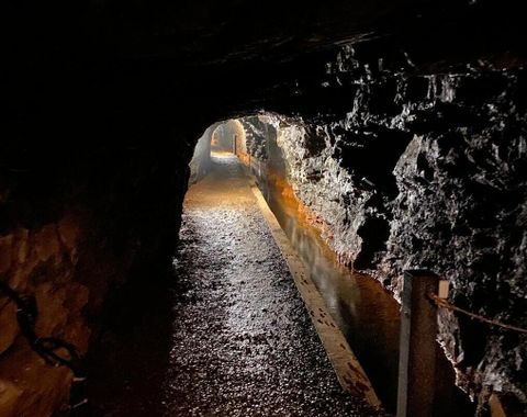 A dark tunnel with damp walls and a narrow watercourse. The light at the end of the tunnel creates a mysterious effect.