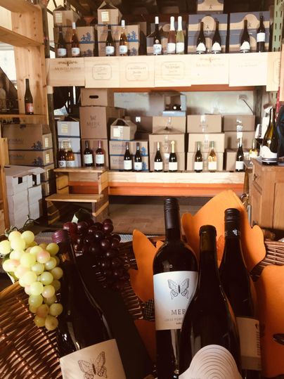 A wine shop with several shelves filled with wine bottles. In the foreground are some wine bottles and grapes.