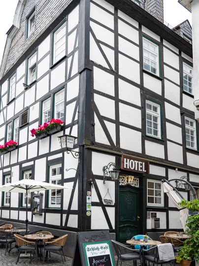 Ein traditionelles Fachwerkhaus mit der Aufschrift „HOTEL“. Draußen stehen Tische und Stühle mit Sonnenschirmen.