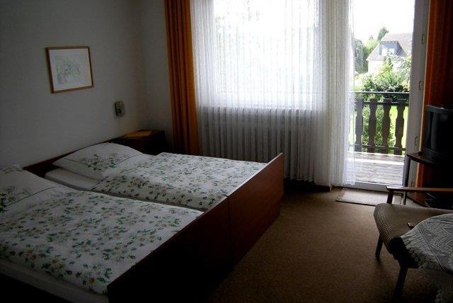 Een eenvoudige slaapkamer met twee eenpersoonsbedden en een balkon. De kamer heeft grote ramen met gordijnen en een gezellige schommelstoel.