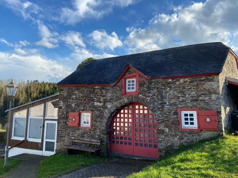Een historisch stenen gebouw met een rode deur en ramen, omringd door groen. Op de achtergrond zijn bomen en een blauwe lucht te zien.