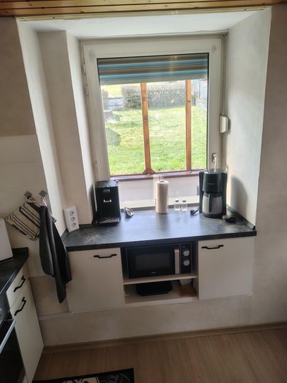 Eine moderne Küche mit einem Fenster, das auf die grüne Wiese blickt. Auf der Arbeitsfläche stehen eine Kaffeemaschine, ein Wasserkocher und eine Mikrowelle.