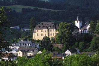A picturesque village with historic buildings and a church. In the background, green hills and trees can be seen.