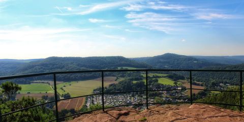 Eine malerische Aussicht von einer Felsplattform, die über grüne Hügel und Felder blickt. Der Himmel ist klar und blau, ideal für einen verträumten Tag in der Natur.